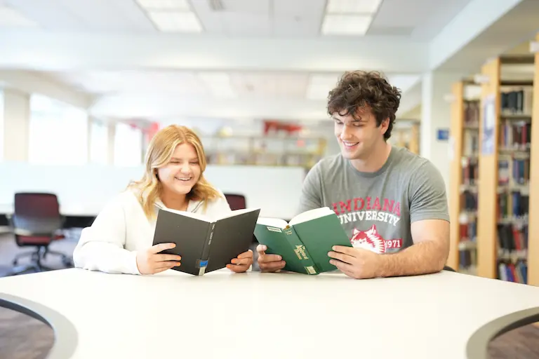 Two students sitting at a table reading a book.