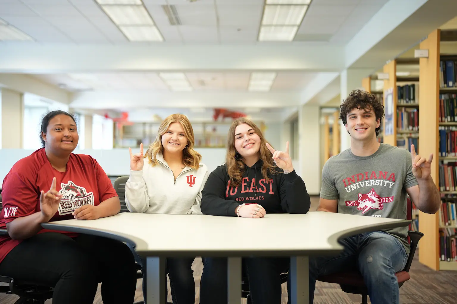 Four students sitting at a table making a peace sign.