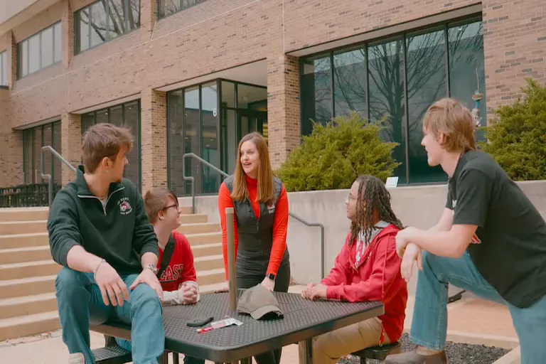 Five students sitting outside at a table talking.