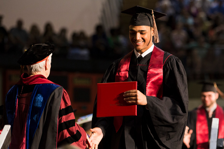 A delighted graduate takes the diploma and goes for a handshake