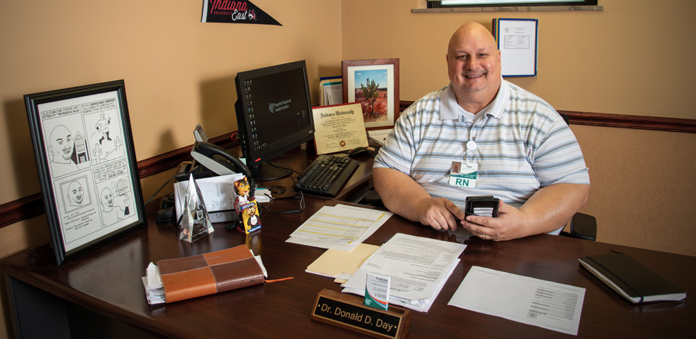 Dr. Donald Day sitting at his desk surrounded by Indiana University East swag.