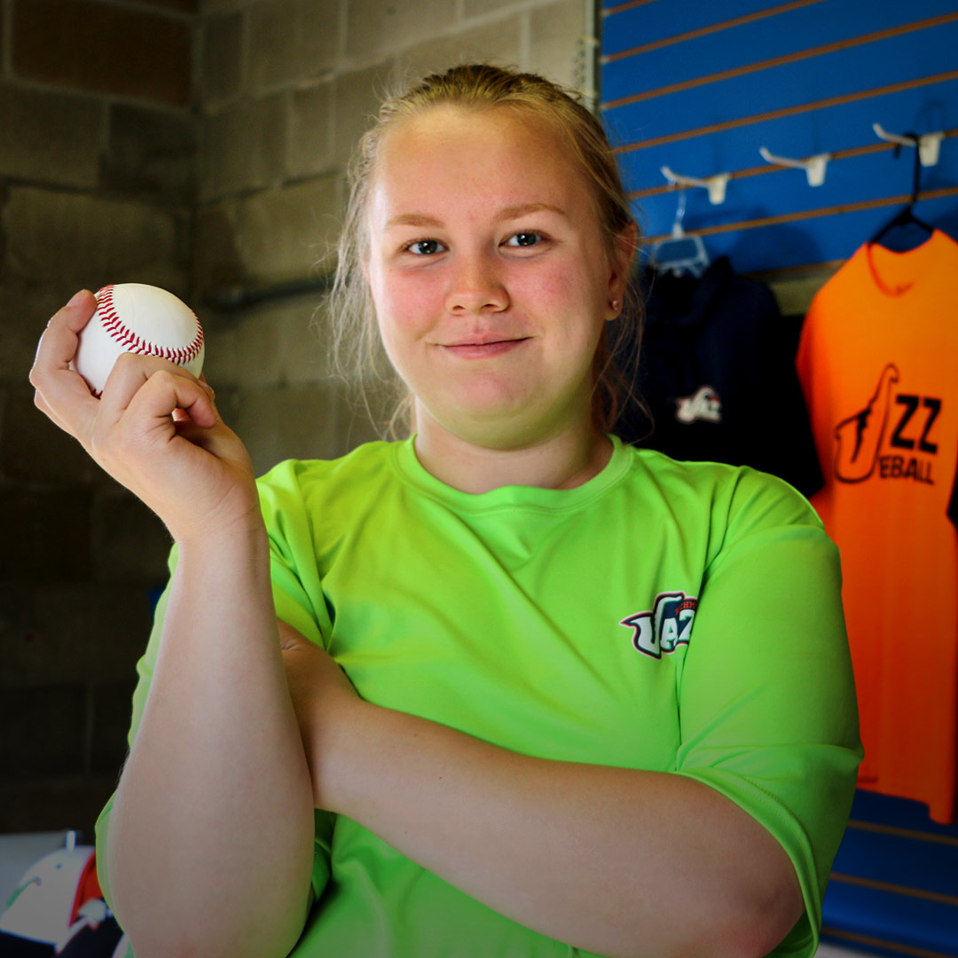 Tiani Christian smiling and holding a baseball in the Richmond Jazz baseball team ticket booth.