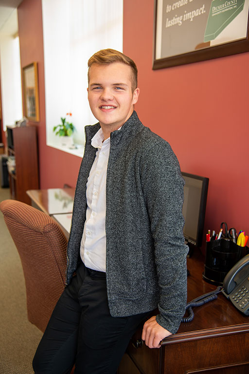 Alex smiling and leaning against his desk.
