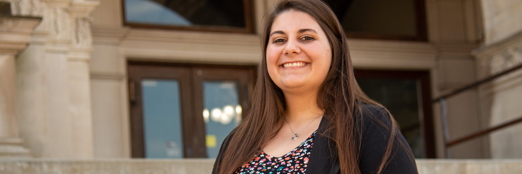 Caysey standing and smiling on the steps of the Rush County courthouse.